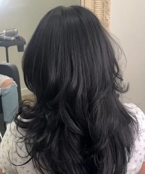 A woman with long black hair sitting in front of a mirror